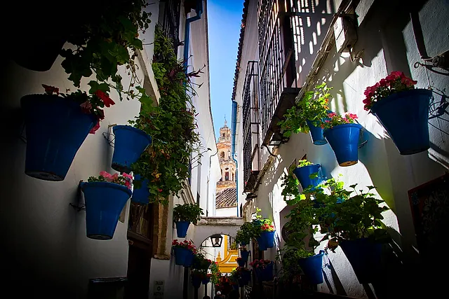 The Calleja de las Flores, a narrow whitewashed lane in Córdoba with blue flowerpots on the walls and the bell tower of the Mosque-Cathedral at the end