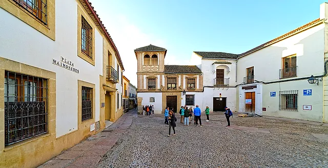 A cobbled square in the Jewish Quarter of Córdoba, with white and ochre houses and a few people crossing it